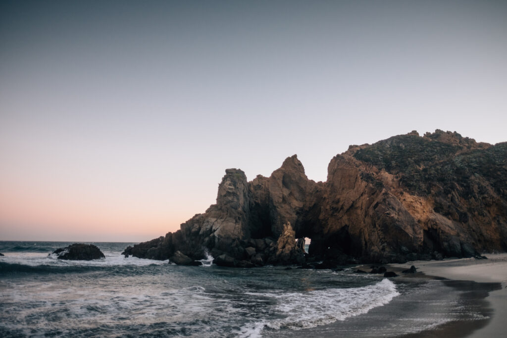 Twilight coastal landscape with rocky cliffs gentle waves and warm to cool gradient sky wallpaper