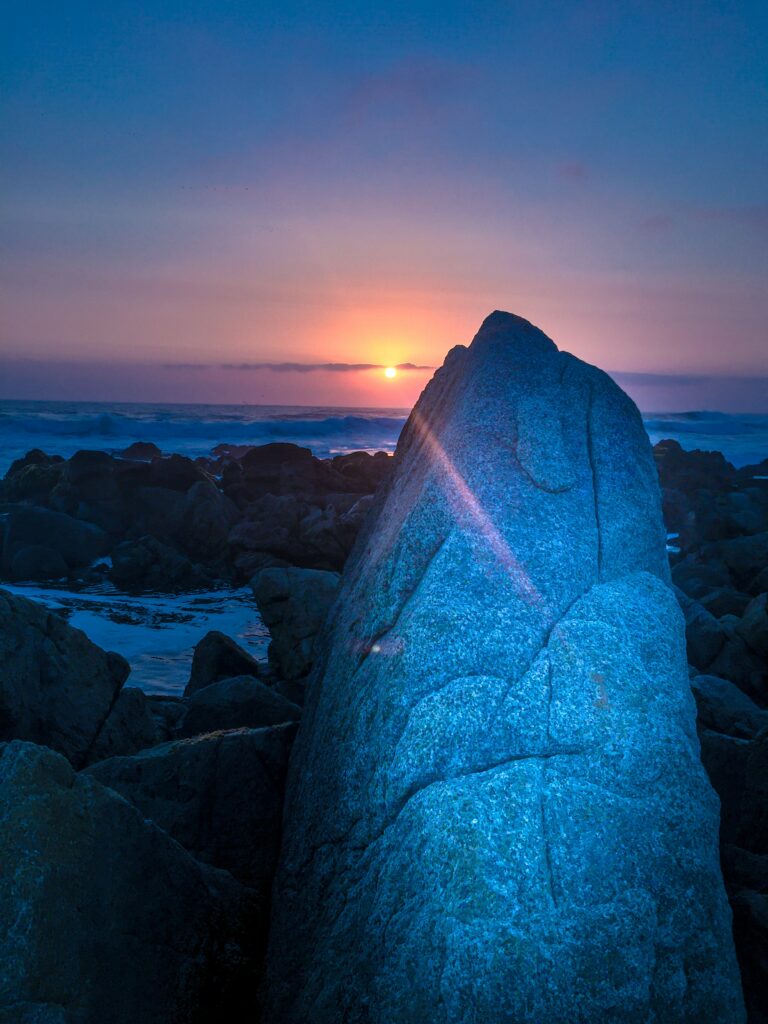 Twilight coastal wallpaper with rugged rocks glowing under warm orange sunset and blue sea hues