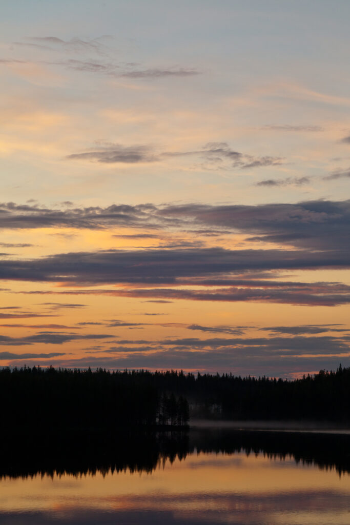 Twilight lake scene with tree silhouettes reflecting on calm water under orange purple sky Wallpaper
