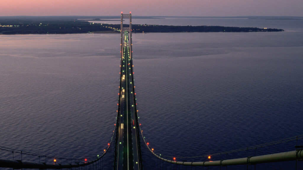 Twilight Over Mackinac Bridge: Tranquil View with Evening Traffic and City Lights Wallpaper