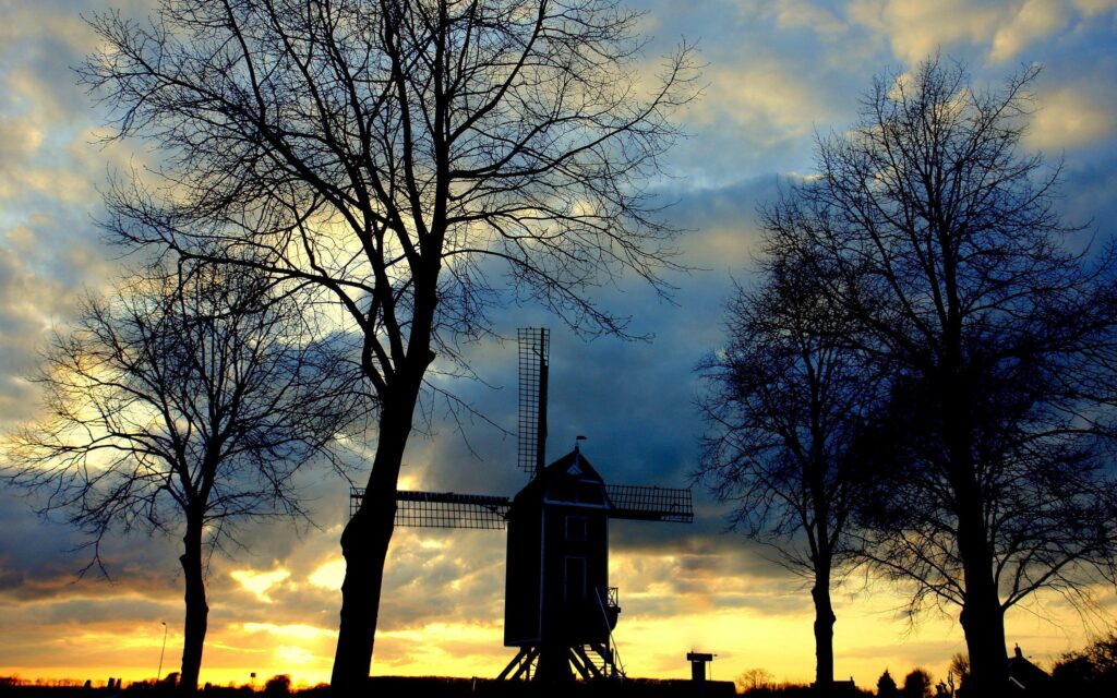 Silhouette of classic mill framed by leafless trees at twilight with vibrant evening sky wallpaper