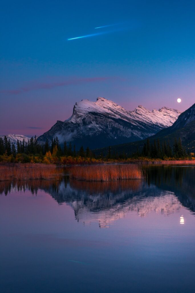 Twilight mountain landscape with snow peaks lake reflection moon and meteor streak wallpaper background