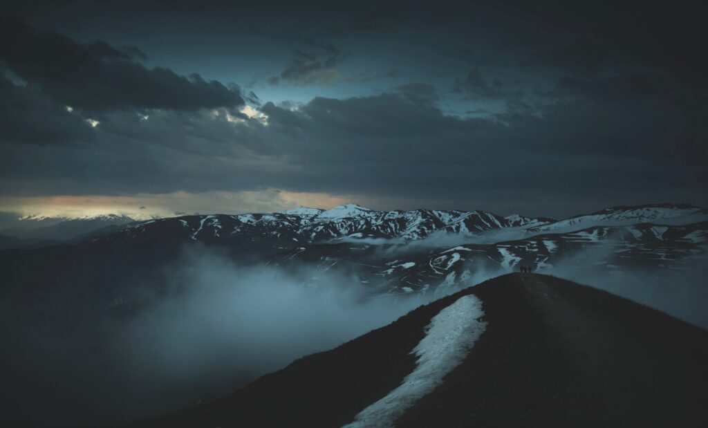 Rugged mountain peaks in twilight fog with snow contrast and glowing horizon background wallpaper