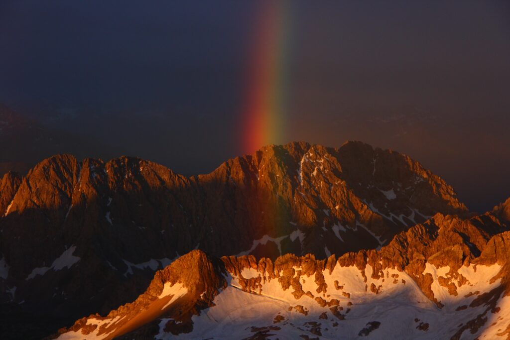 Snowy rugged mountain peaks under twilight sky with vibrant rainbow and golden sunlight wallpaper