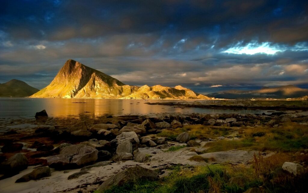 Twilight mountain reflection in calm lake with golden light on rocks and lush grass landscape Wallpaper