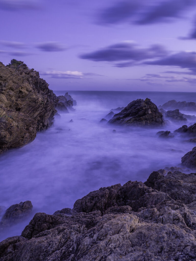 Twilight seascape with rugged rocks waves misty spray soft blue purple hues long exposure wallpaper