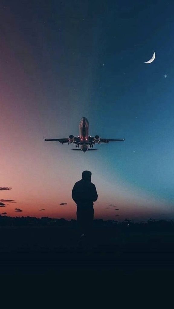 Silhouette of man watching jet in twilight sky with moon and blue orange gradient wallpaper