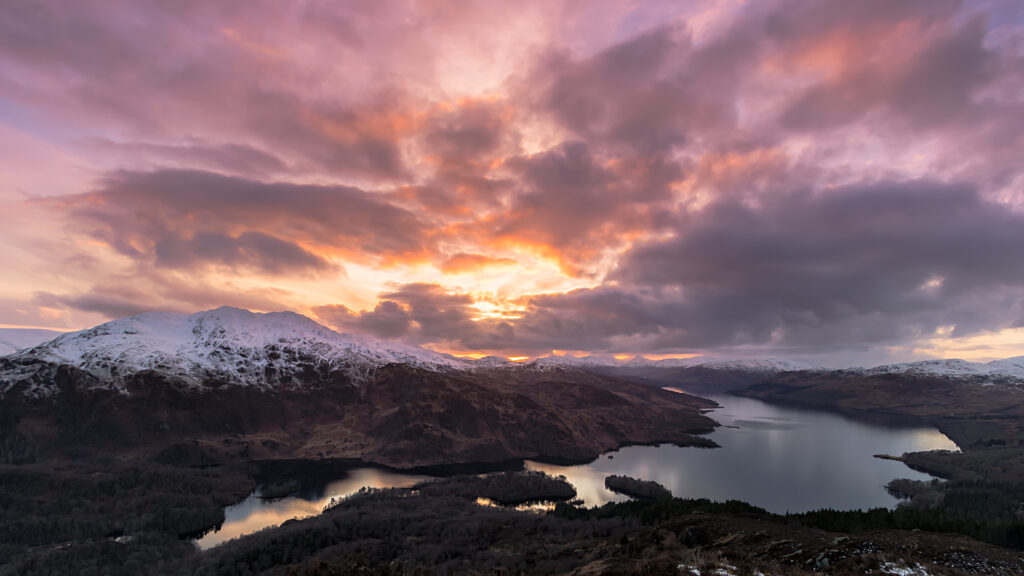 Aerial view of snow-capped mountains and serene lake under vibrant colorful twilight sky wallpaper