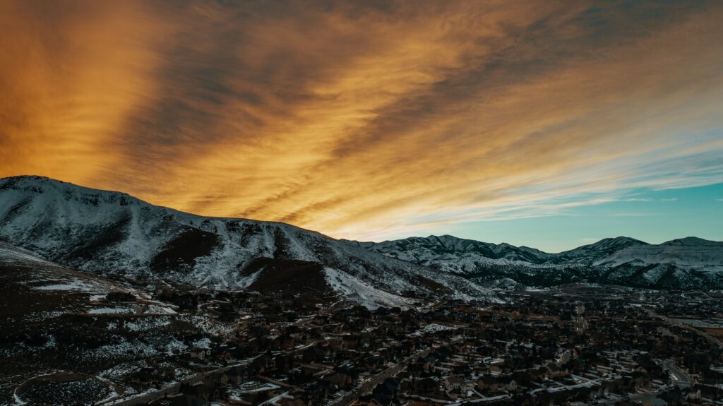 Aerial view of peaceful village surrounded by snow-capped mountains at twilight with warm sky Wallpaper