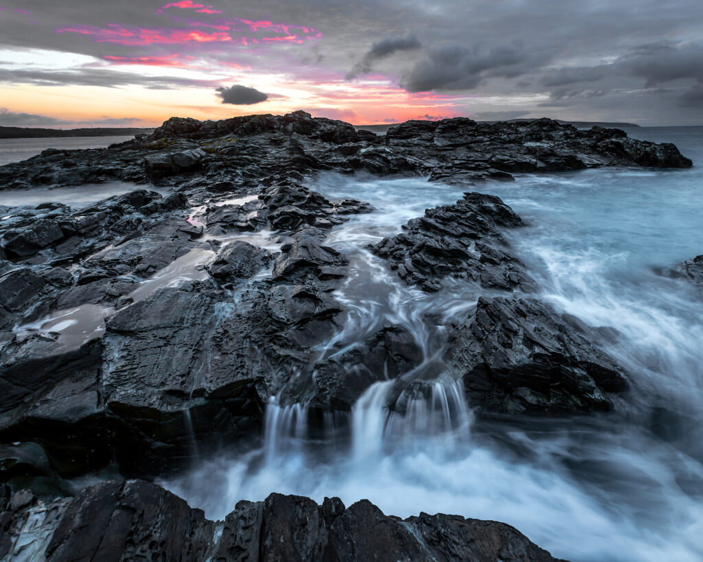 Rugged rocks and flowing waterfall under vibrant pink and orange twilight sky wallpaper background