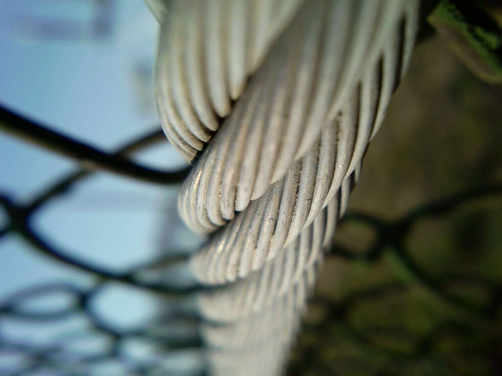 Twisted Silver Metal Wire Close-Up with Blurred Wire Fence Background Wallpaper