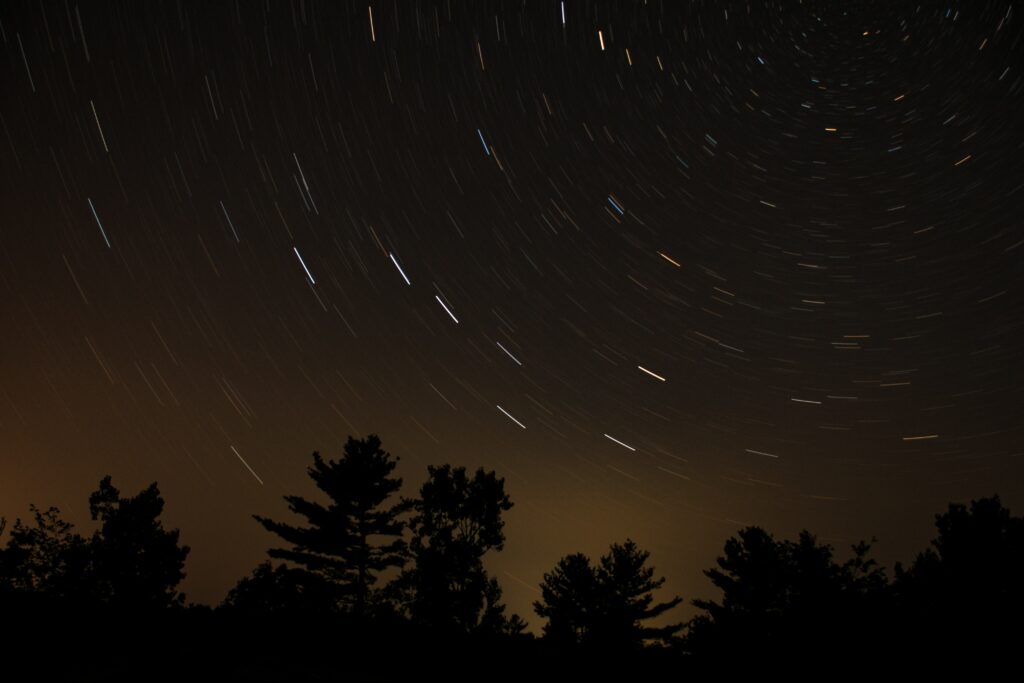 Swirling star trails over silhouetted trees in a dusky night sky long exposure wallpaper background