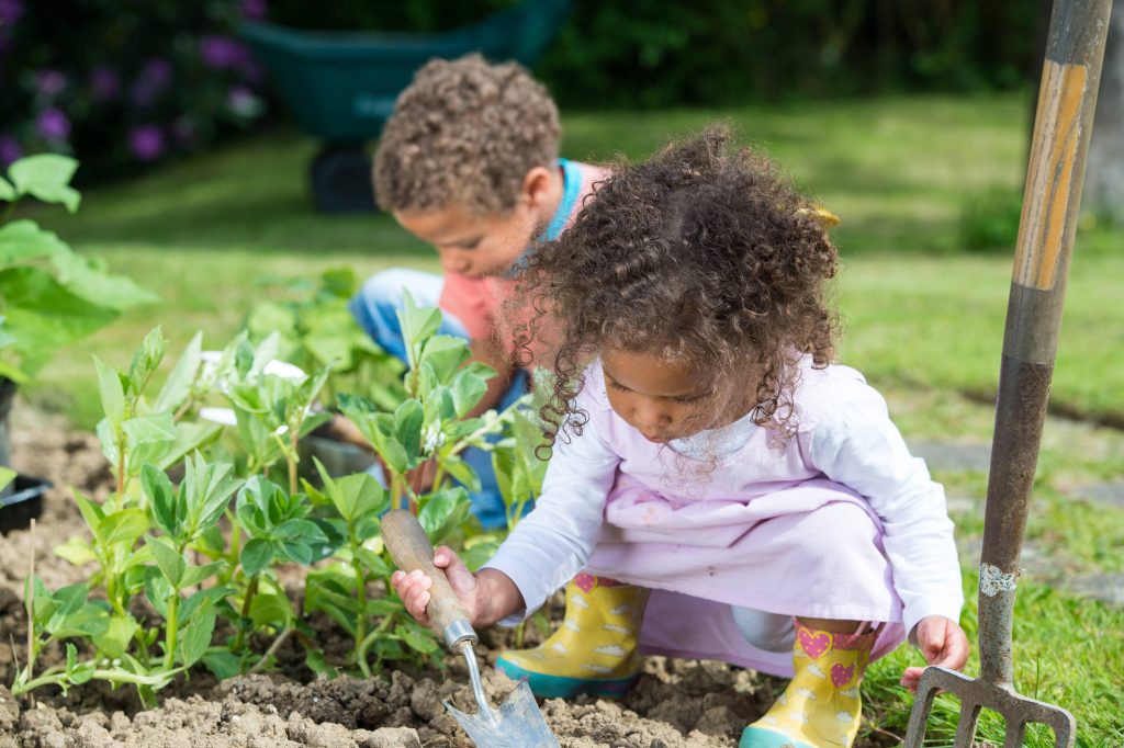 Two children gardening outdoors bright spring scene girl with yellow boots plants greenery Wallpaper