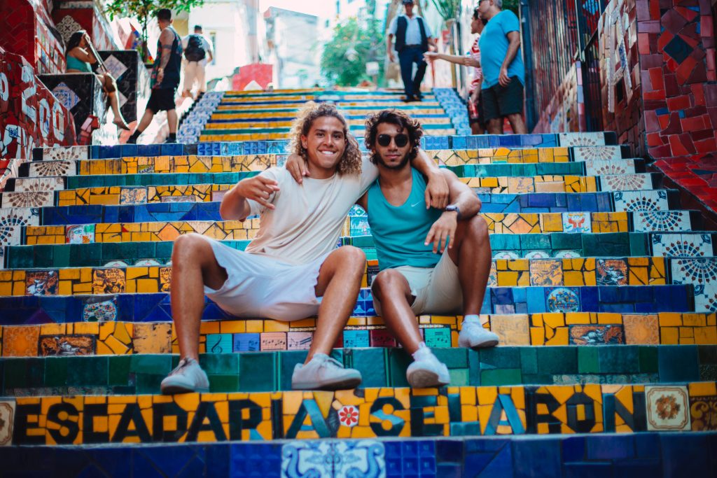 Two friends smile sitting on colorful mosaic tiles of Escadaria Selarón steps in Rio Brazil Wallpaper