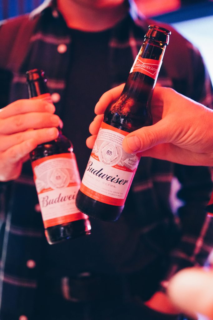 Two hands clinking Budweiser beer bottles celebrating festive nightlife with warm glowing light Wallpaper