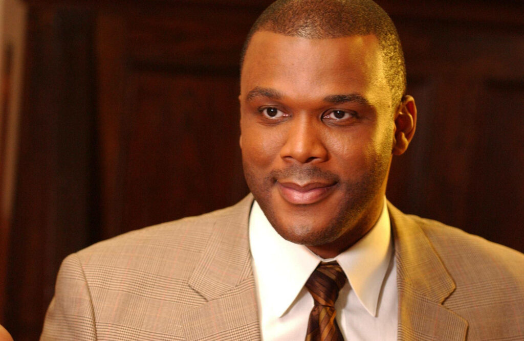 Tyler Perry in beige checked suit and brown tie polished look dark background wallpaper