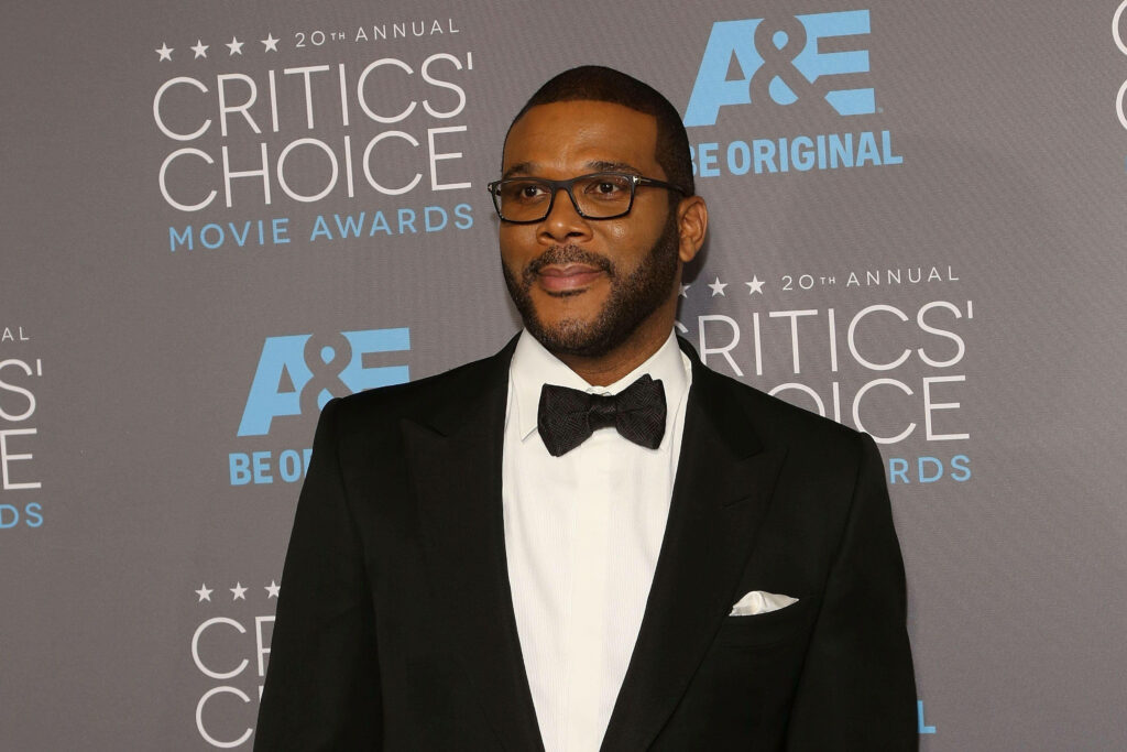 Tyler Perry in tuxedo confidently posing on Critics Choice Movie Awards red carpet background Wallpaper