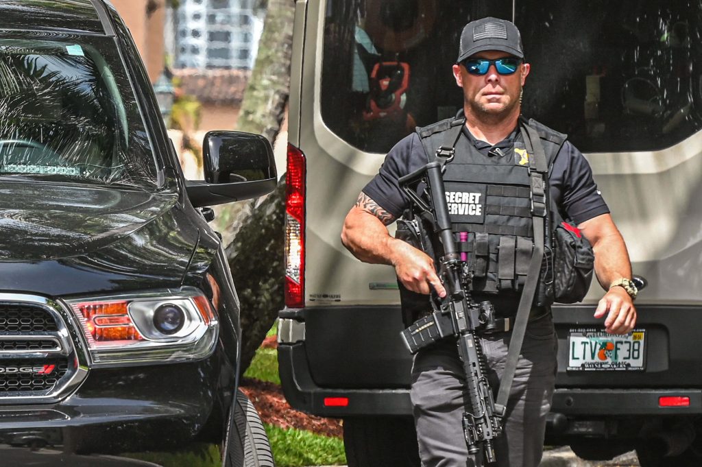 US Secret Service agent in tactical gear with rifle patrolling near security vehicles HD wallpaper