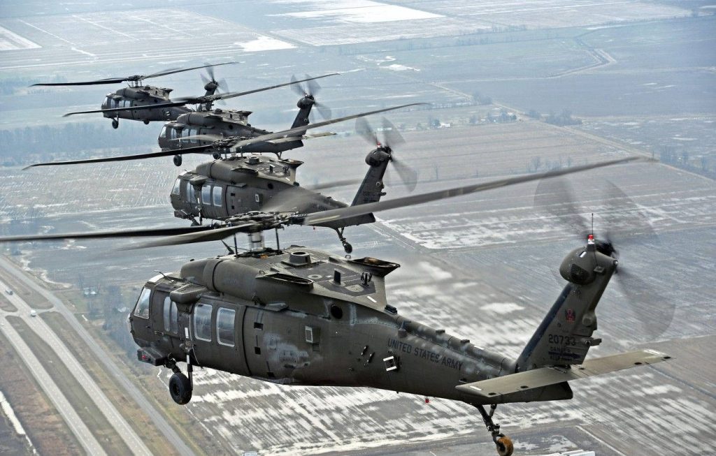 Four U.S. Army UH-60 Black Hawk helicopters flying in formation over snowy rural highway Wallpaper