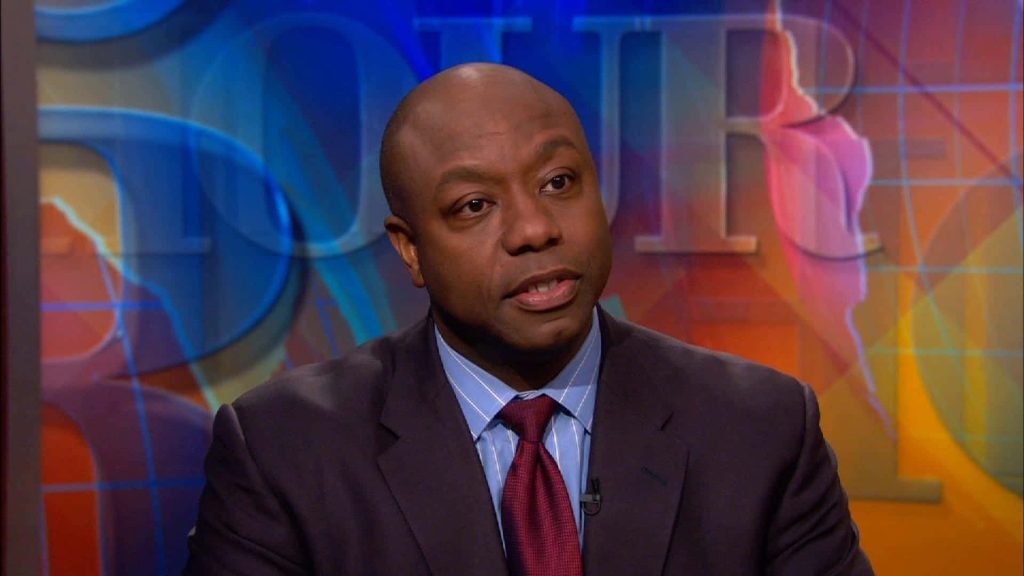 U.S. Senator Tim Scott in studio wearing suit and maroon tie with vibrant news wallpaper background