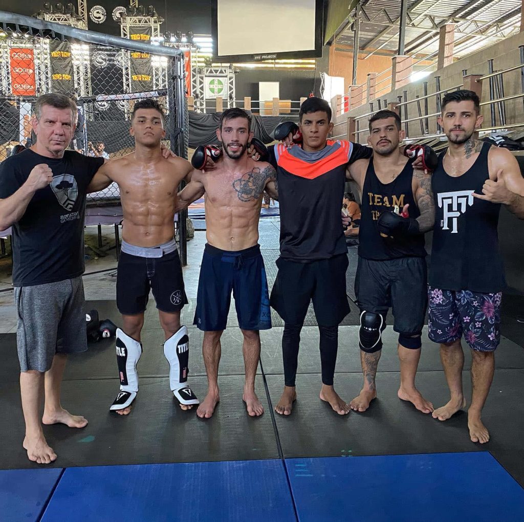 UFC fighter Matheus Nicolau with his MMA training team inside gym octagon cage background Wallpaper