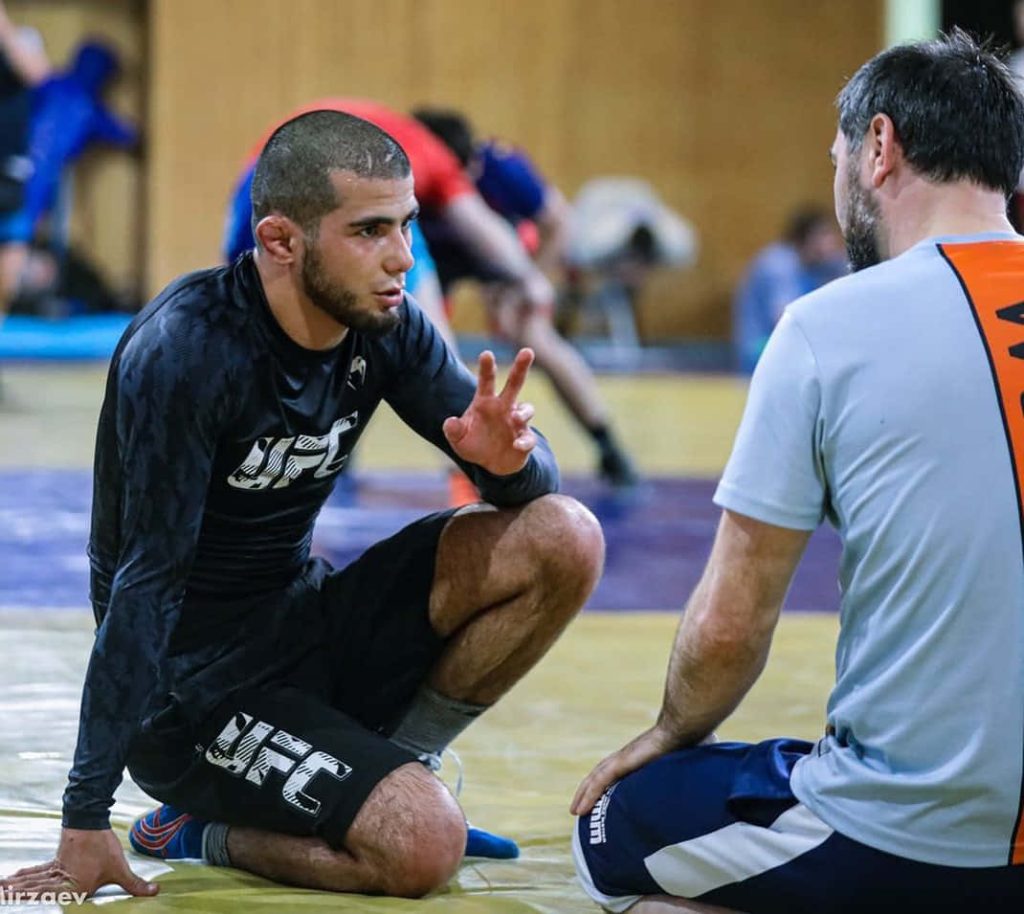 UFC rising star Muhammad Mokaev kneeling on gym mat training with coach in professional MMA gear Wallpaper