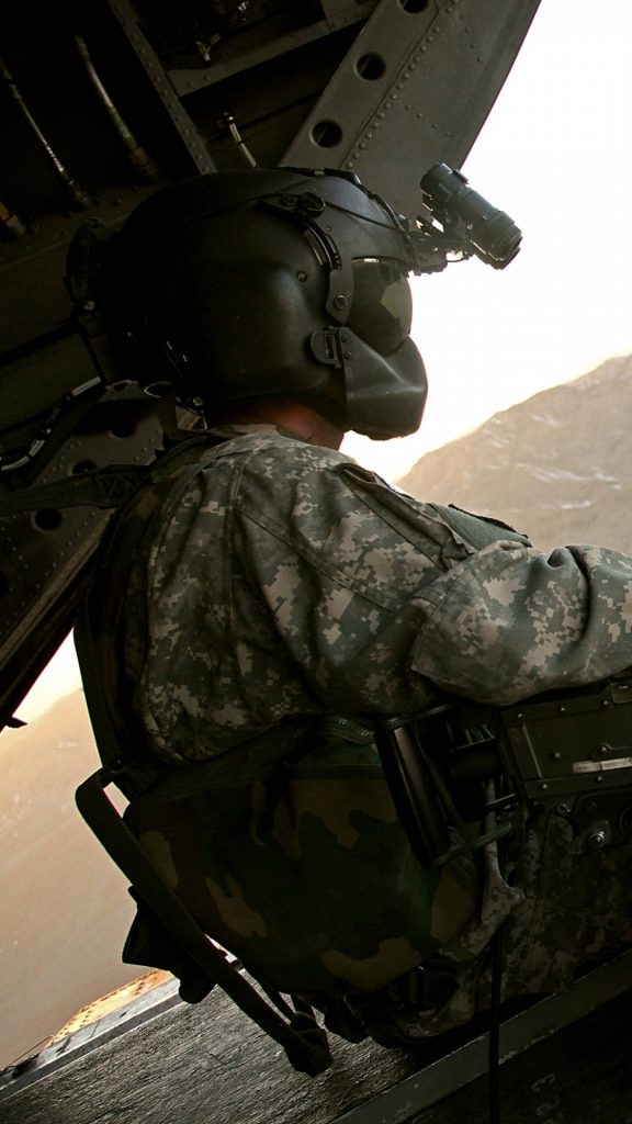 US Army door gunner in UCP camo watches rugged mountains from helicopter cabin war wallpaper