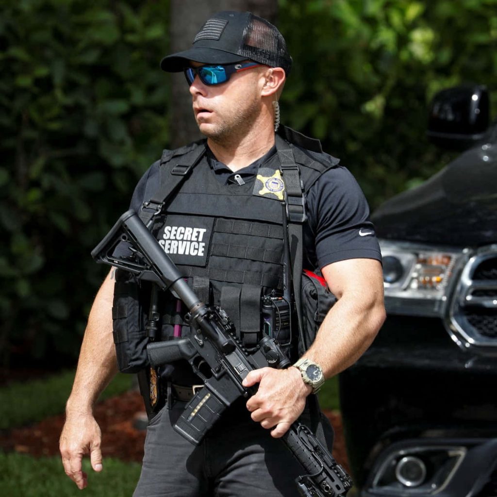 US Secret Service agent in tactical gear with rifle standing by black vehicle outdoors wallpaper
