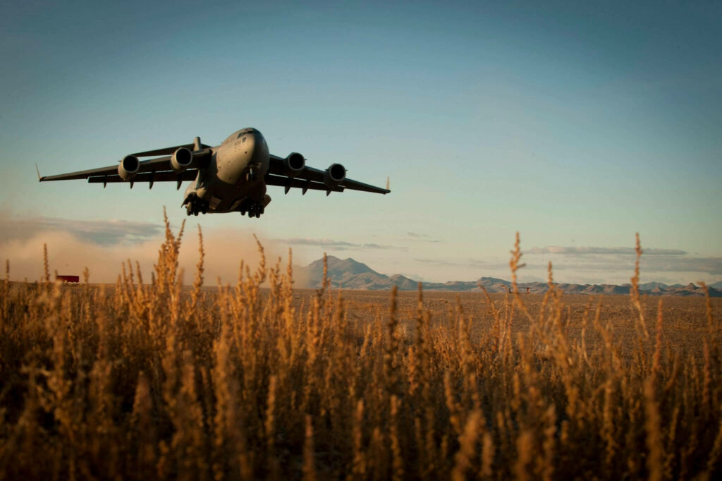 USA military aircraft flying low over rugged Afghan field mountains golden grasses clear sky Wallpaper