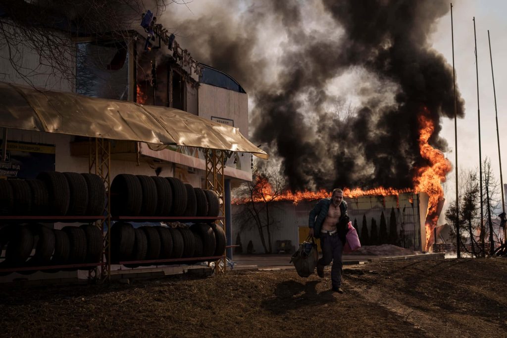 Civilian fleeing burning building in Ukraine amid thick smoke and intense flames war photography Wallpaper