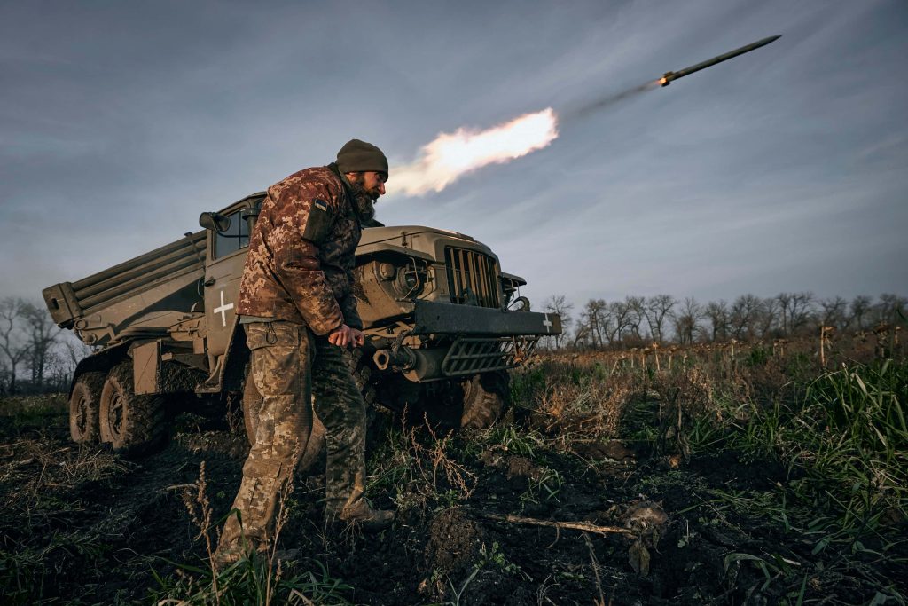 Ukrainian soldier firing BM-21 Grad rocket launcher on muddy battlefield under overcast sky Wallpaper