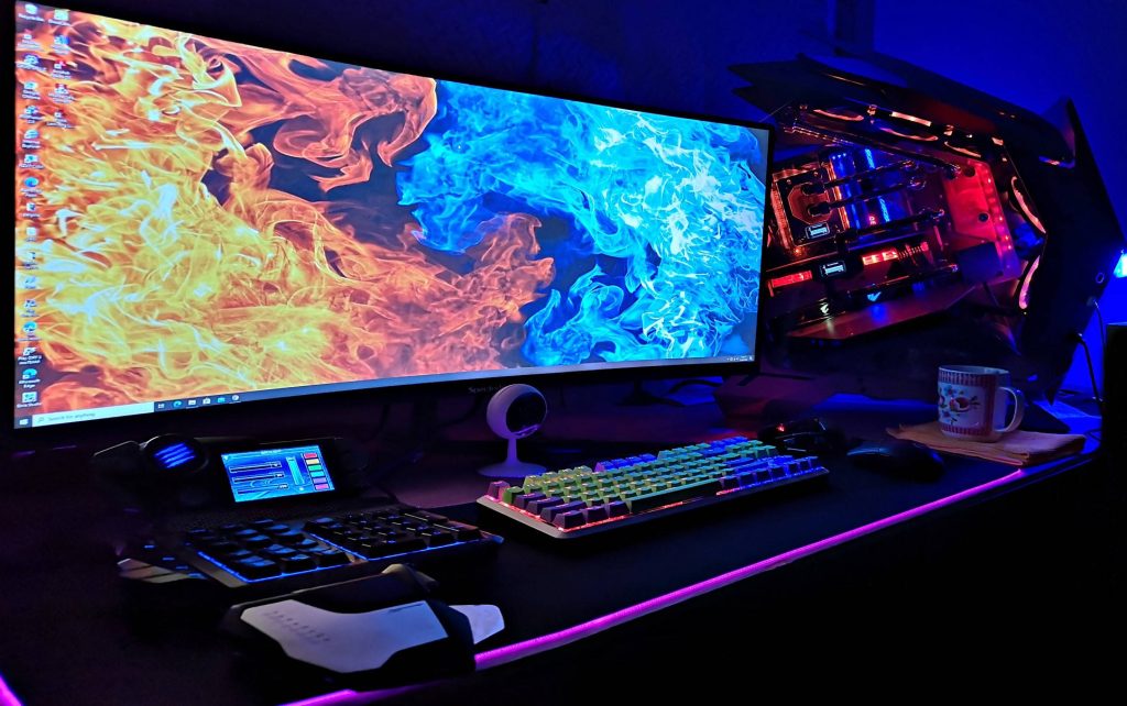 Vibrant gaming room with ultrawide curved monitor fire ice wallpaper RGB lighting and mechanical keyboard