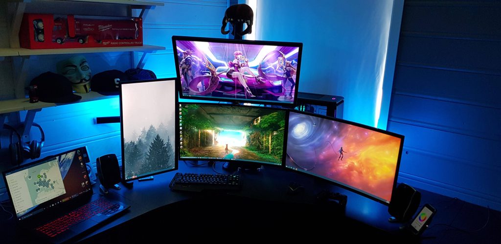 Advanced multi-monitor gaming setup with blue ambient lights showing League of Legends KDA art and nature wallpapers