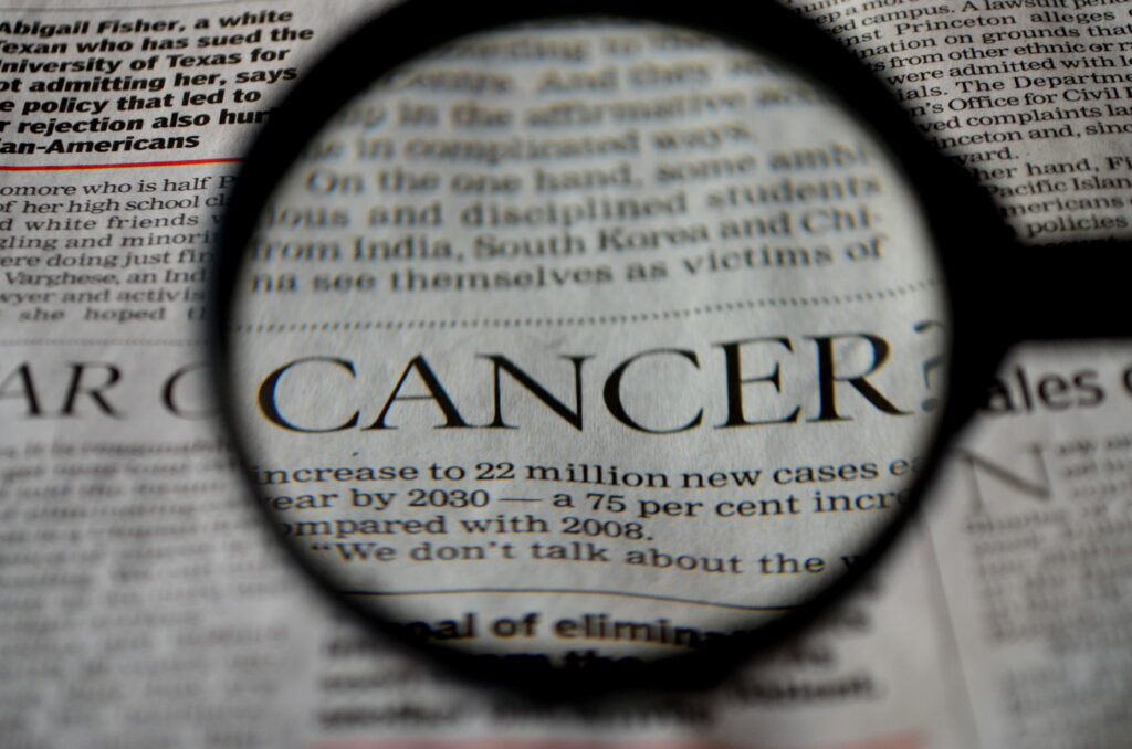 Macro photo of magnifying glass highlighting cancer text in newspaper for health research Wallpaper