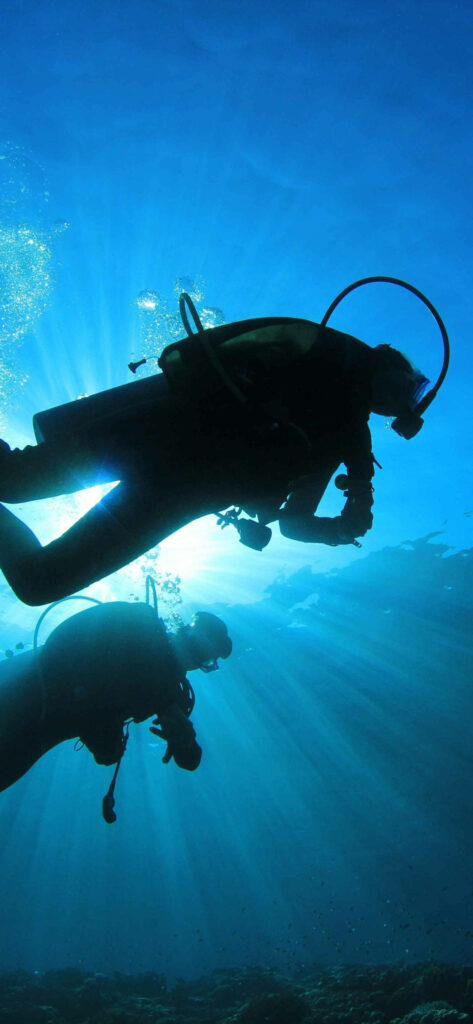 Two scuba divers underwater with vibrant blue light rays in an ocean exploration wallpaper background