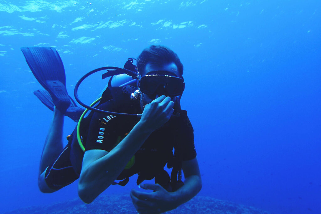 Scuba diver exploring vibrant deep blue ocean with shimmering light rays underwater wallpaper background