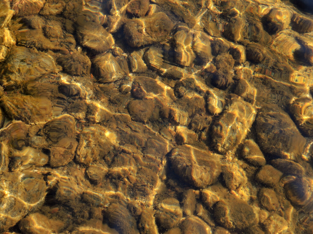 Underwater stones and pebbles with sunlight reflections creating warm shimmering patterns wallpaper
