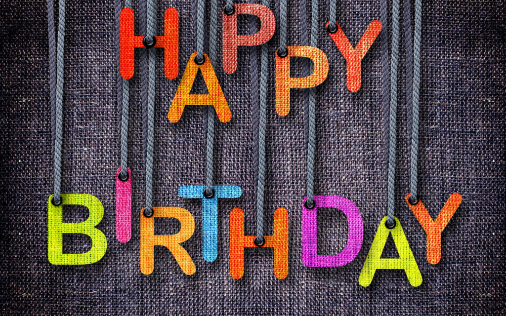 Festive birthday wallpaper with colorful fabric letters hanging on rustic burlap background
