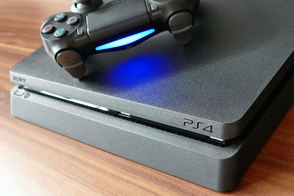 Close-up of matte black Sony PS4 Slim with DualShock 4 glowing blue light on wood surface Wallpaper