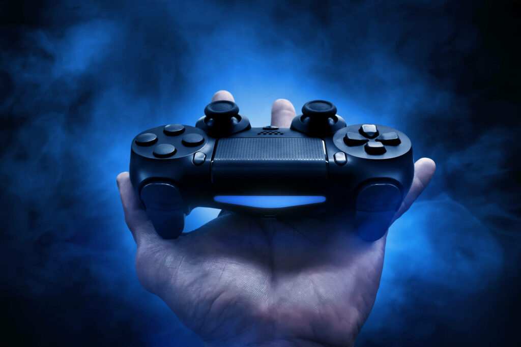 Empowering Gamers: A Mighty Hold on a Black Gaming Controller amidst a Blue Misty Gaming Realm Wallpaper