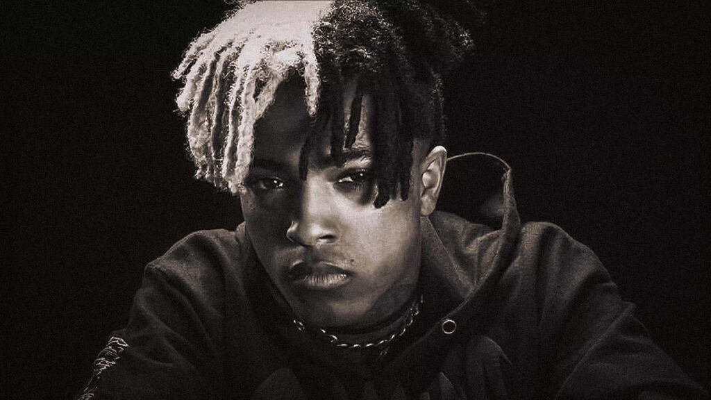 Monochrome portrait of late rapper XXXTentacion with half-bleached dreadlocks and intense gaze Wallpaper