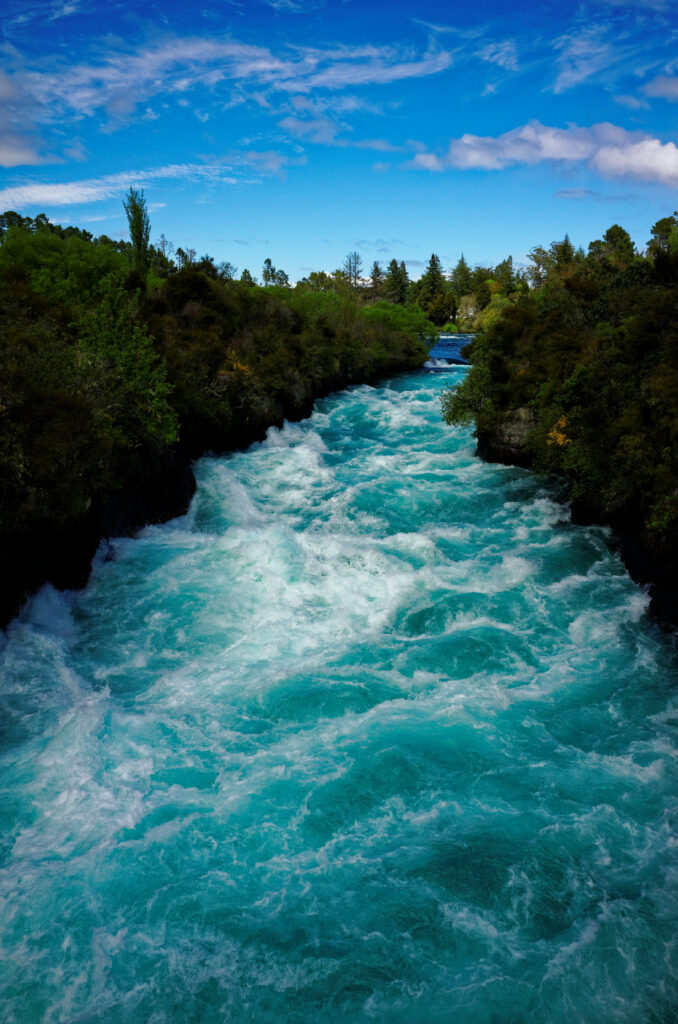Vibrant rushing river with frothy blue waves flowing through lush green forest under bright sky Wallpaper