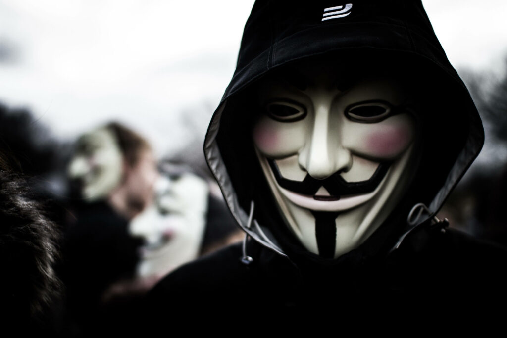 Unveiling the Anonymous Mastermind: High-Resolution 4k Shot of the Masked Hacker's Closeup, Surrounded by a Mysterious Band of Blur-speed Hackers Wallpaper