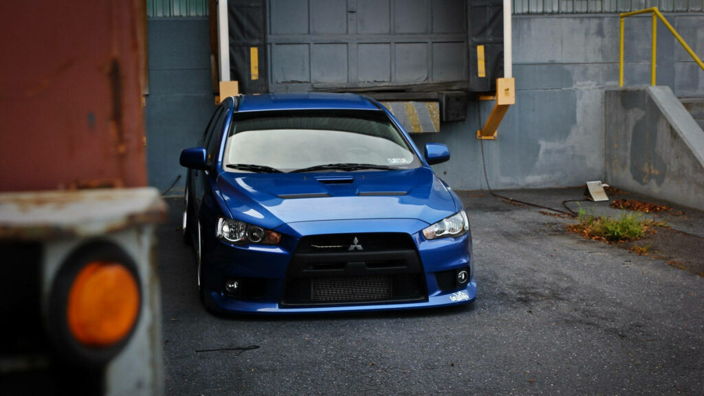Jdm Perfection: Captivating Snapshot of a Striking Blue Mitsubishi Lancer Evolution X Resting in a Spacious Gray Asphalt Garage Wallpaper