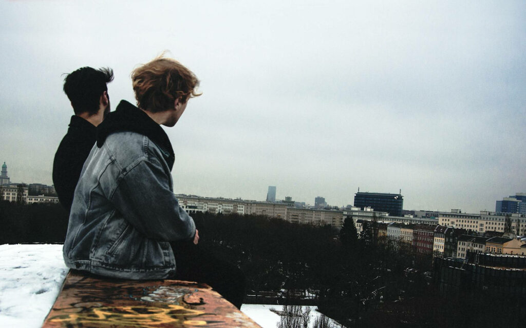 Bonding Over Skylines: Capturing the Friendship of Adorable Boys on a Rooftop Parapet Wallpaper
