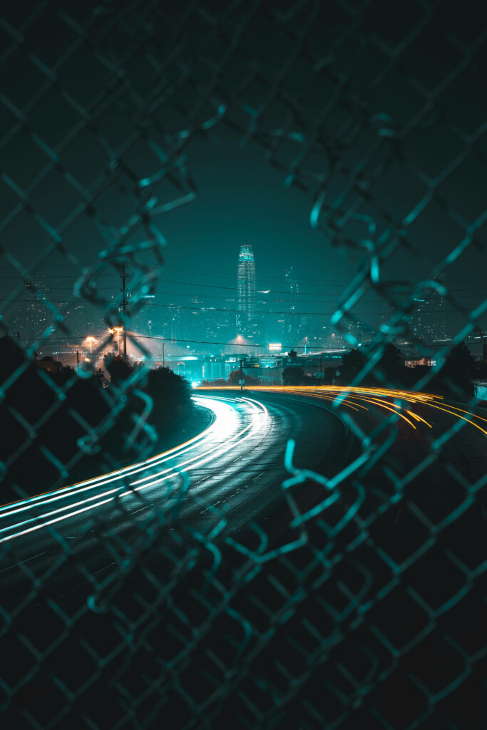 Cityscape Behind Bars: A Chain-Linked Fence Lock Screen Wallpaper for iPhone