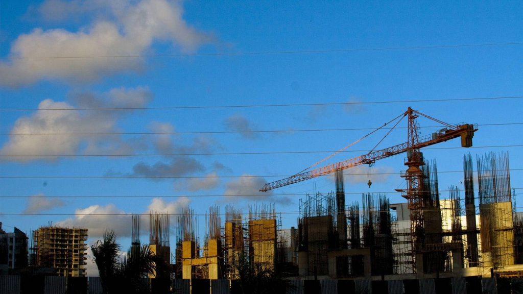 Unfinished concrete buildings with steel rebar and tower crane under blue cloudy sky wallpaper
