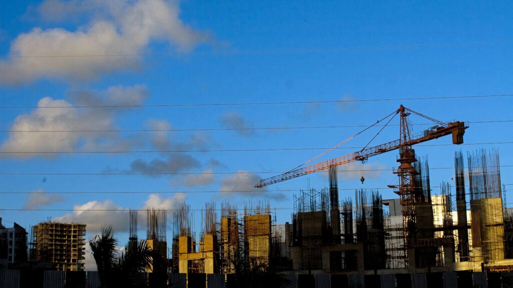 Construction site with crane and concrete structures under bright blue sky showcasing urban development Wallpaper