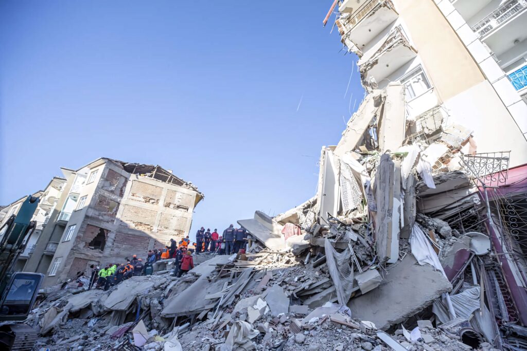 Urban earthquake aftermath with collapsed buildings rescue workers debris resilience hope wallpaper