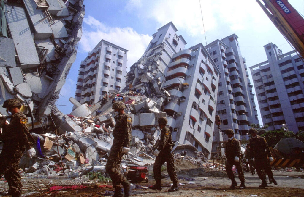 Collapsed high-rise earthquake disaster with military rescue workers amid urban rubble background Wallpaper